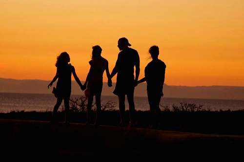 holding hands silhouette of man standing beside shore under brown sky during daytime silhouette